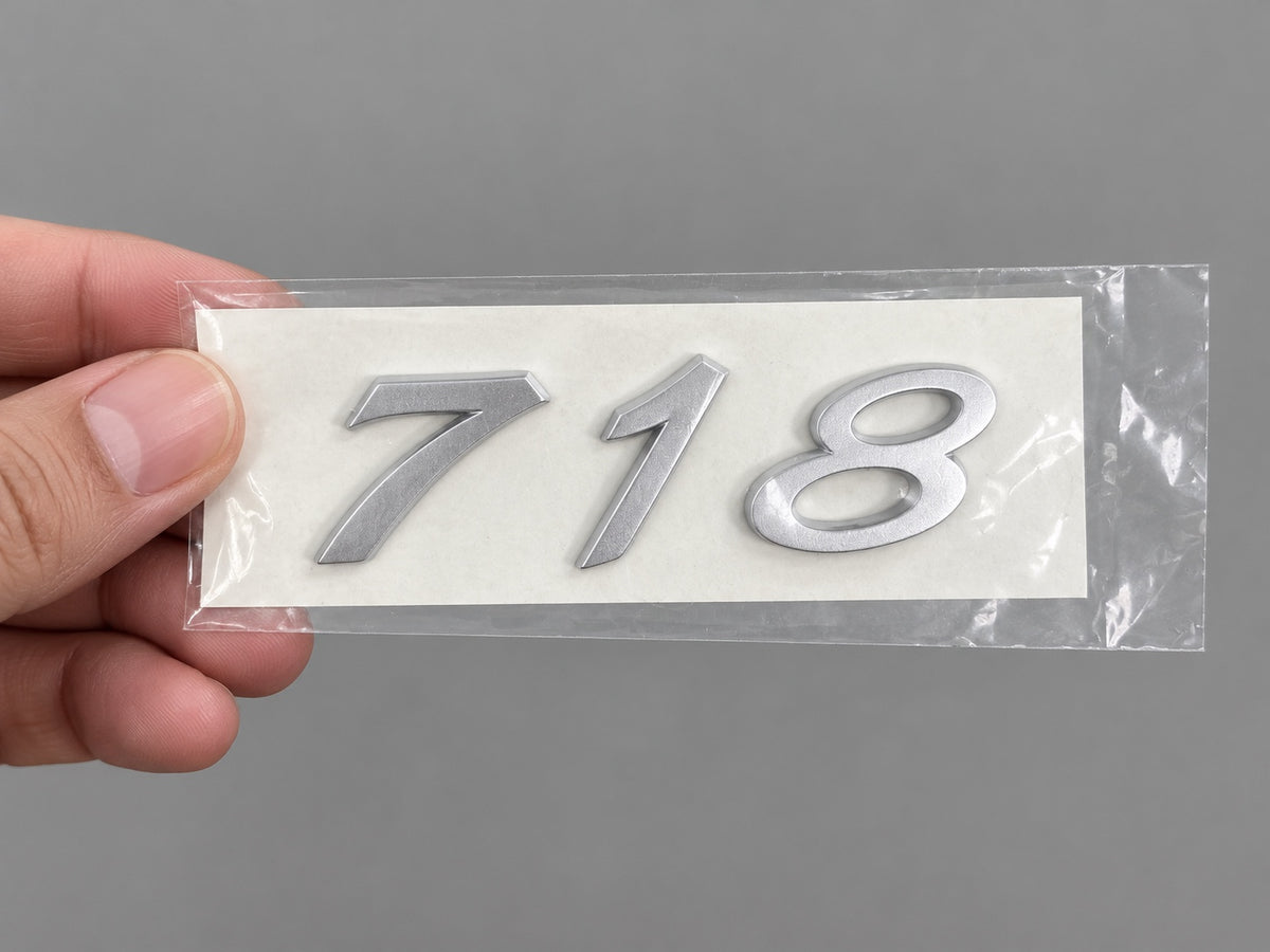Silver-coloured aftermarket 718 badge set in protective packaging