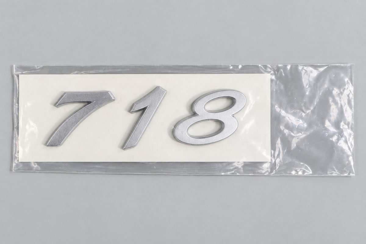 Silver-coloured aftermarket 718 badge set in protective packaging