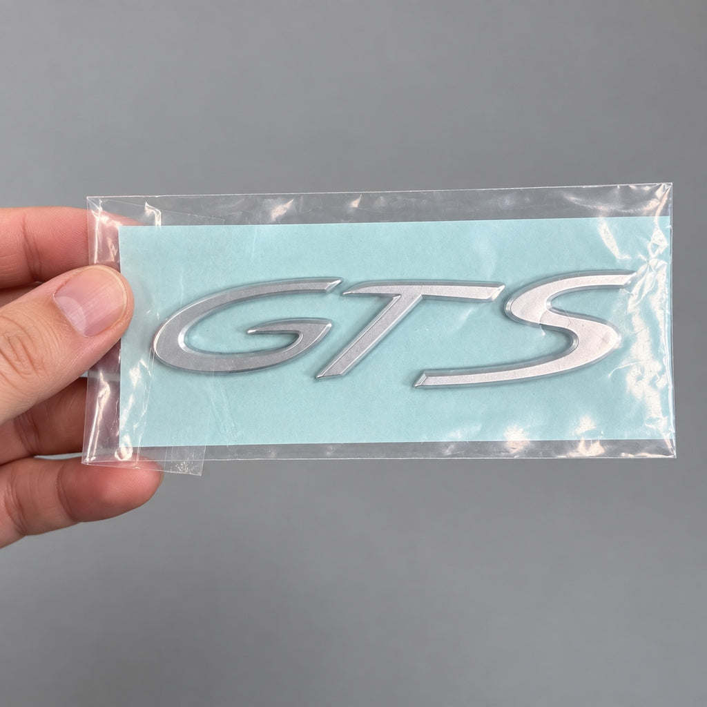 Silver-coloured aftermarket GTS badge set in protective packaging