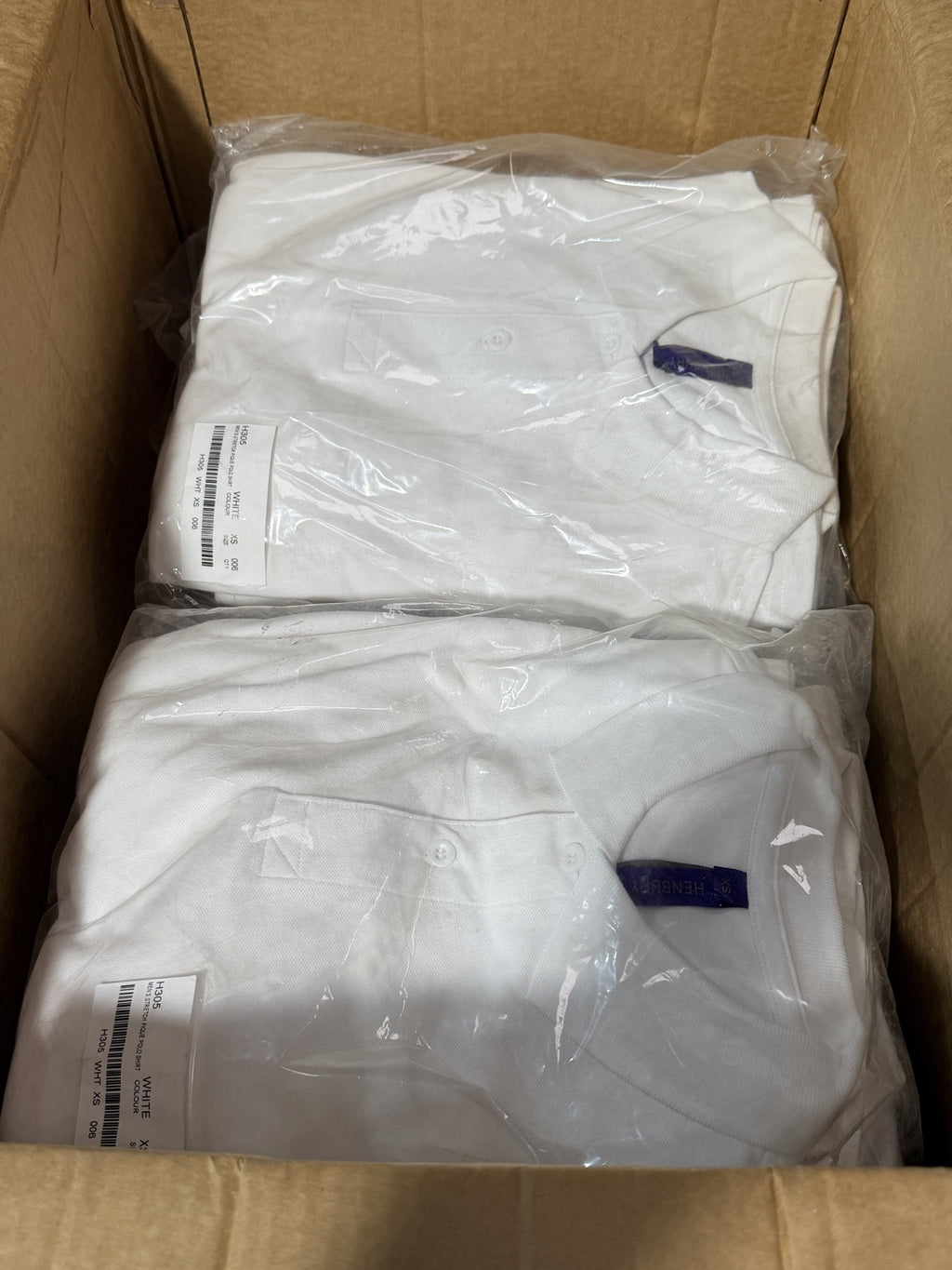 Sealed packs of Henbury H305 white polos in the carton – actual stock